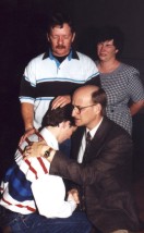 The pastor blesses a young man while his parents pray over him.